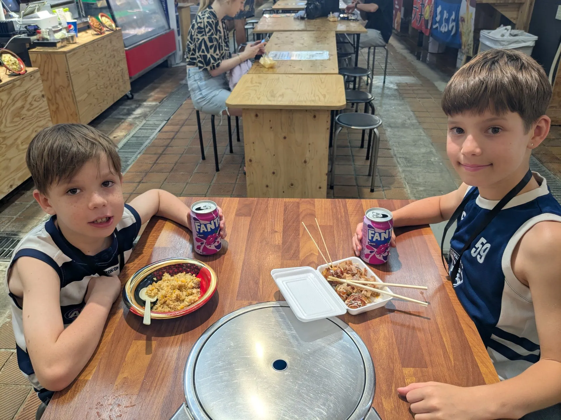 Kids eating takoyaki and okonomiyaki at a food hall in Namba, Osaka
