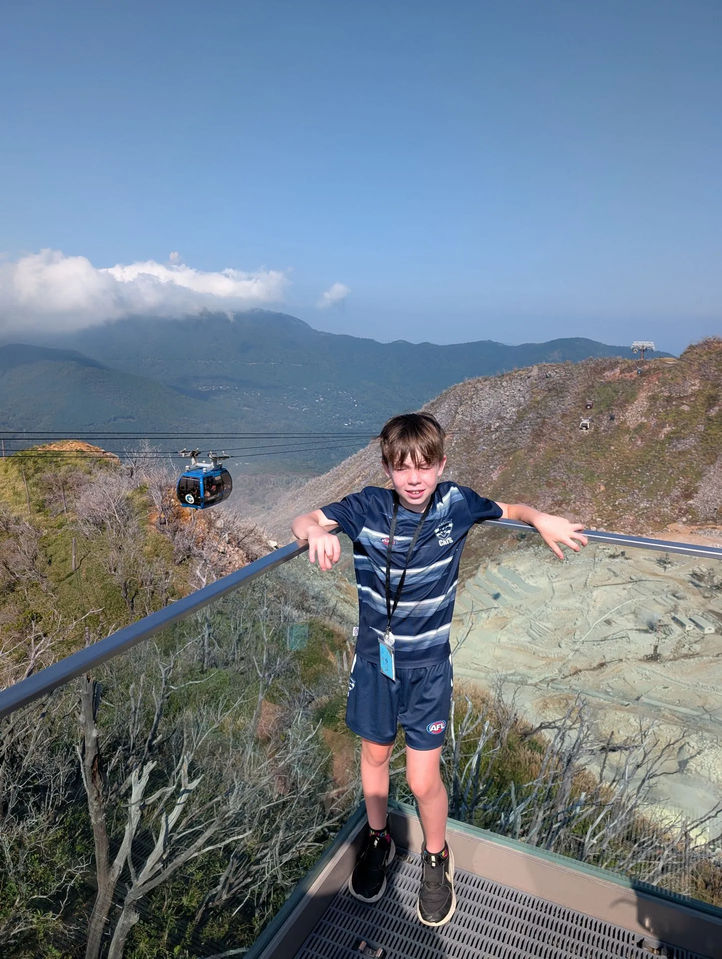 Child posing at Owakudani with ropeway gondolas visible in the background