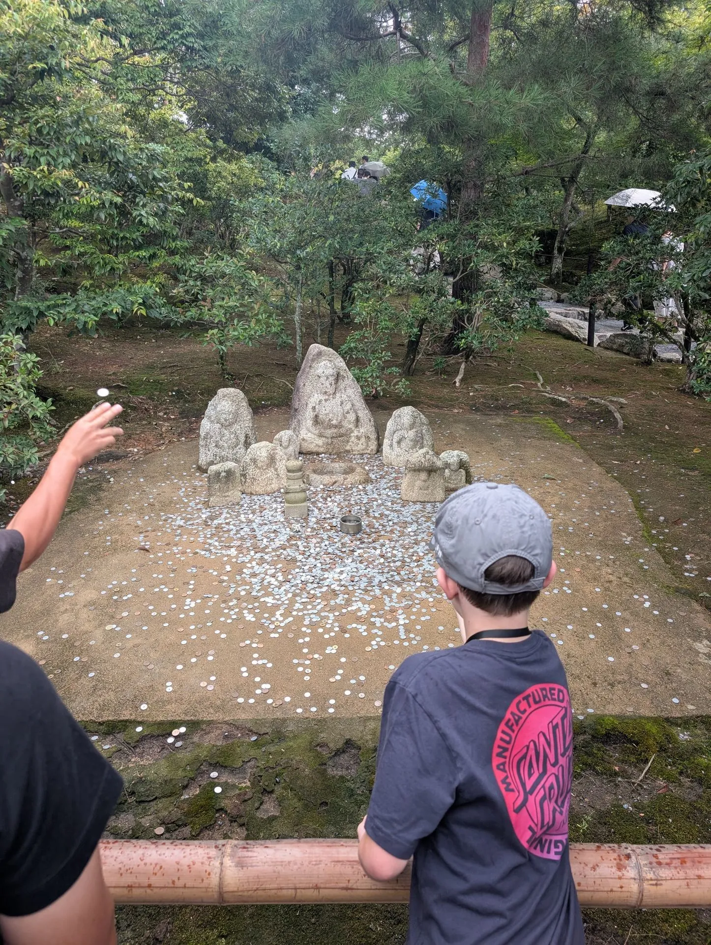 Stone Buddha statues at Kinkakuji garden with visitors tossing coins