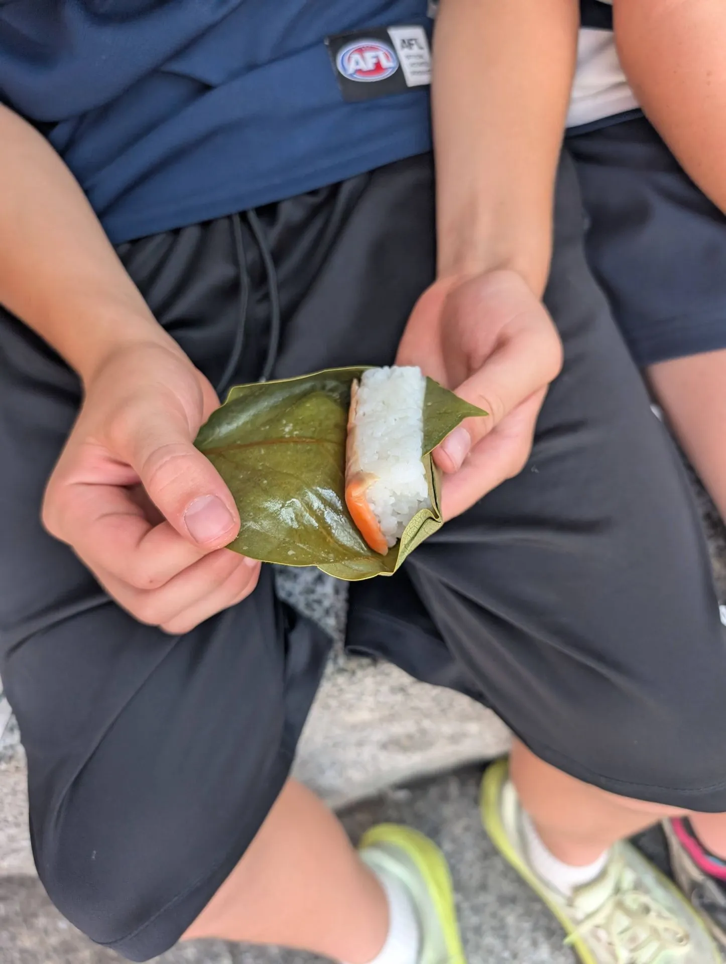 A child's hands unwrapping kakinoha-zushi persimmon leaf sushi to reveal white rice and salmon