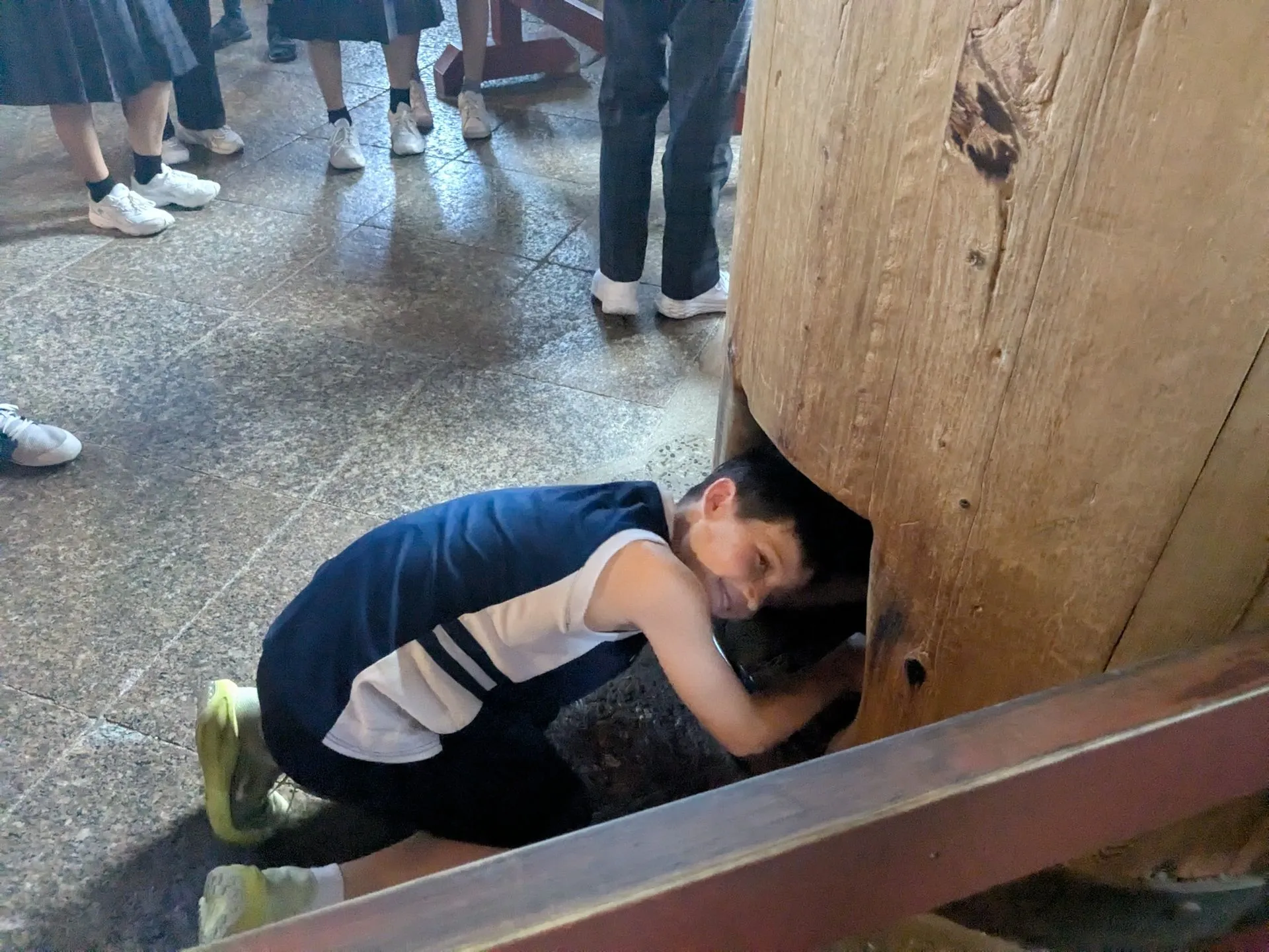 A child crawling through the lucky pillar hole inside Todai-ji temple, smiling at the camera