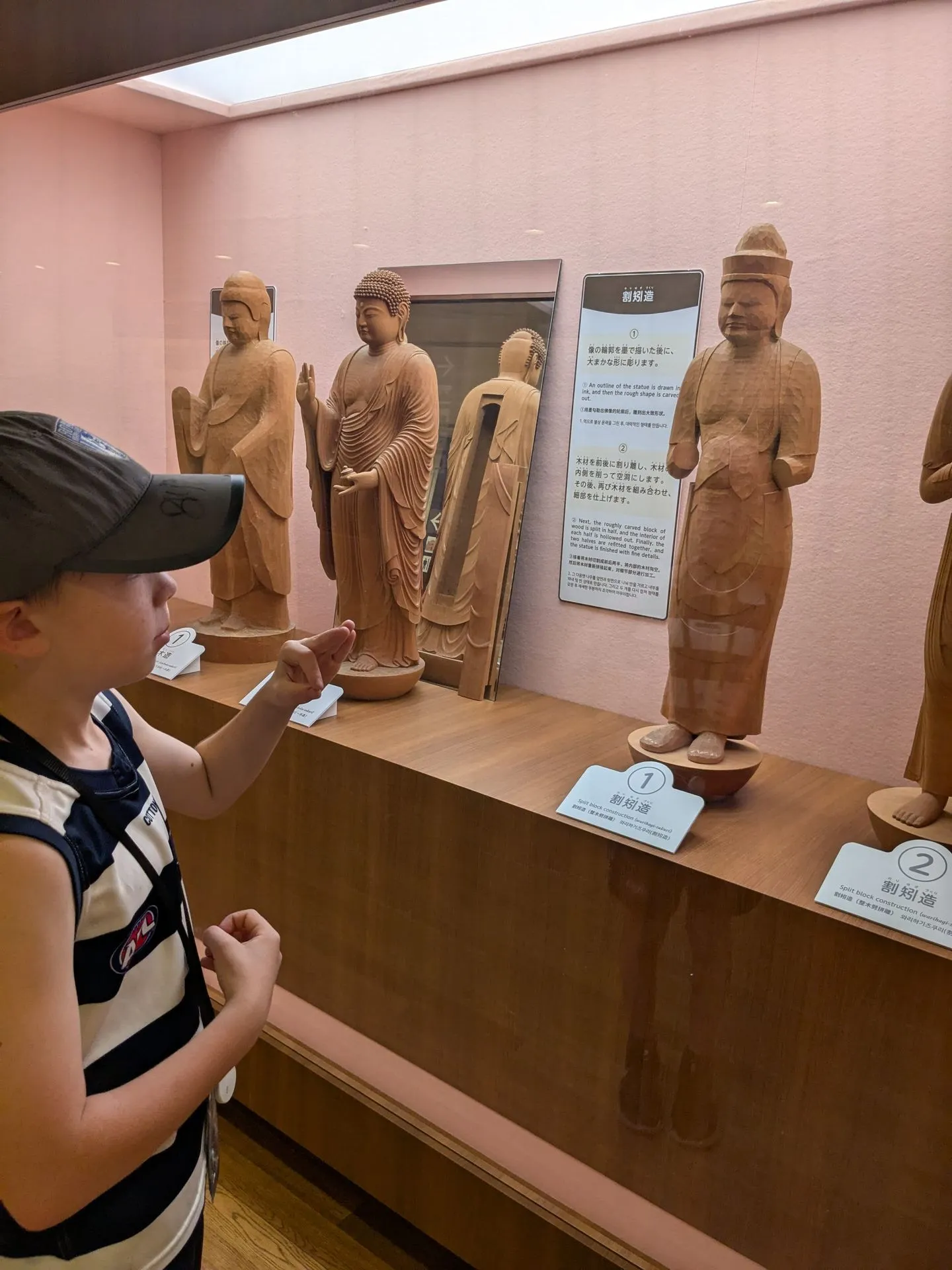 A child examining a wooden Buddhist statue carving exhibit at the Todai-ji Museum, showing the numbered stages of split-block construction