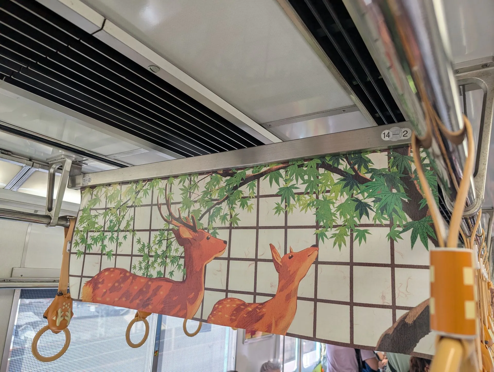 Interior of a train carriage with deer-themed artwork on the overhead advertising panels, showing two sika deer under maple trees