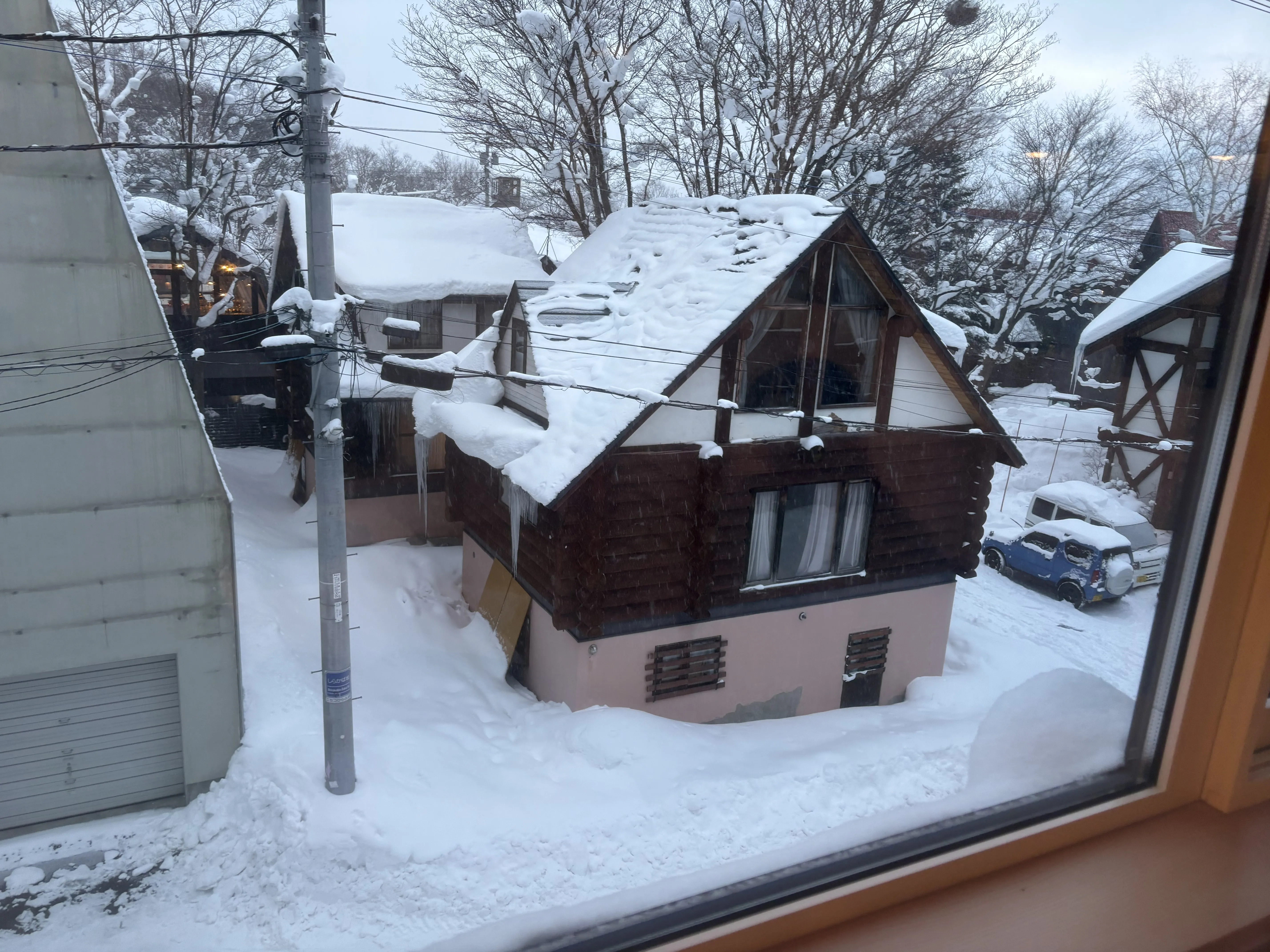 A Niseko chalet and cars buried in deep snow, seen from an apartment window