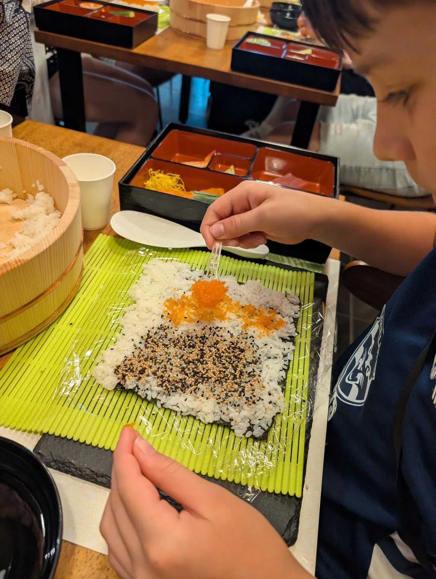 Child rolling sushi at a Tokyo sushi making class with guidance from instructor