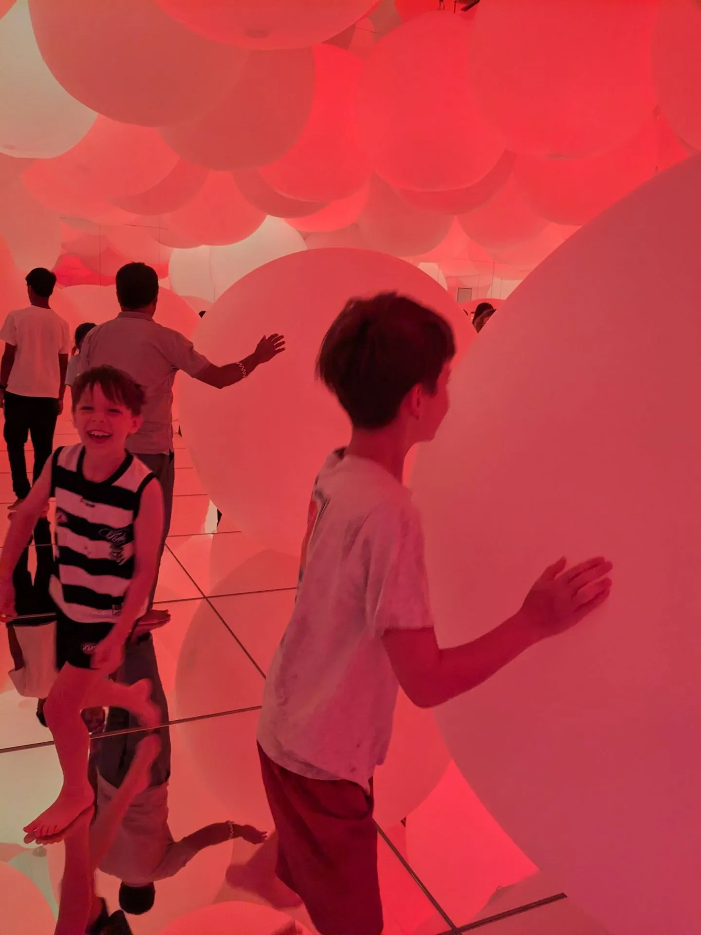 Child playing among hundreds of red balloons in a TeamLab Planets installation